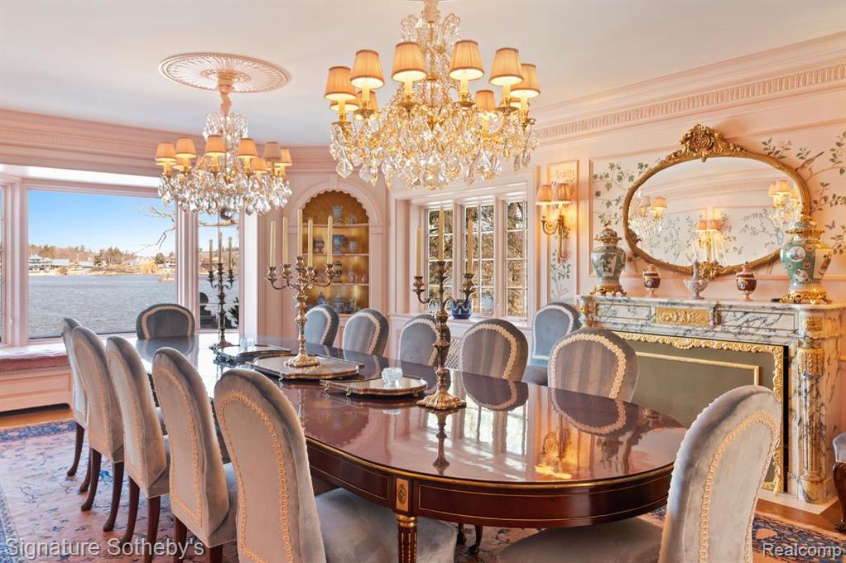 Dining room with a round table, chairs, chandelier and a glass window.