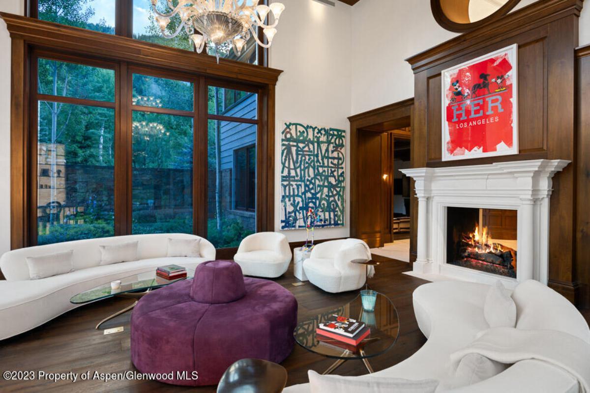 Living room with couches, glass walls, fireplace and a wooden floor.
