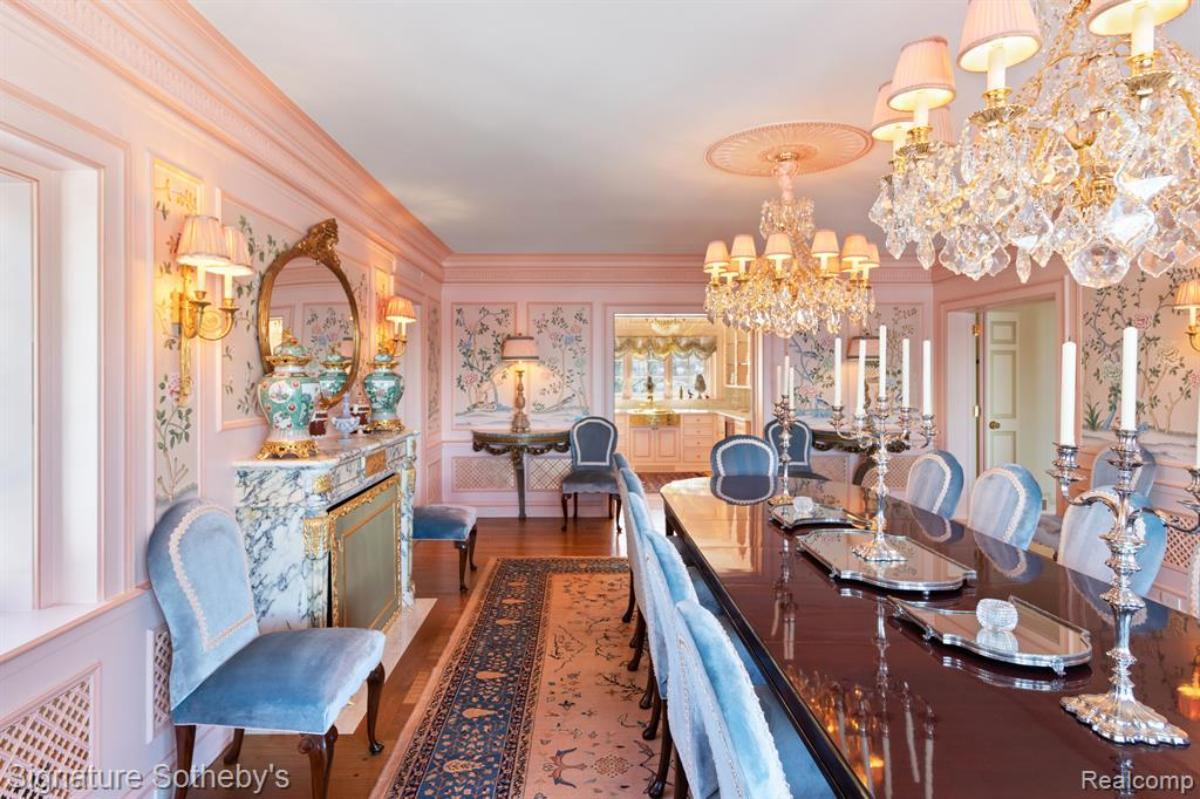 Dining room with a round table, chairs, chandeliers and a large rug,