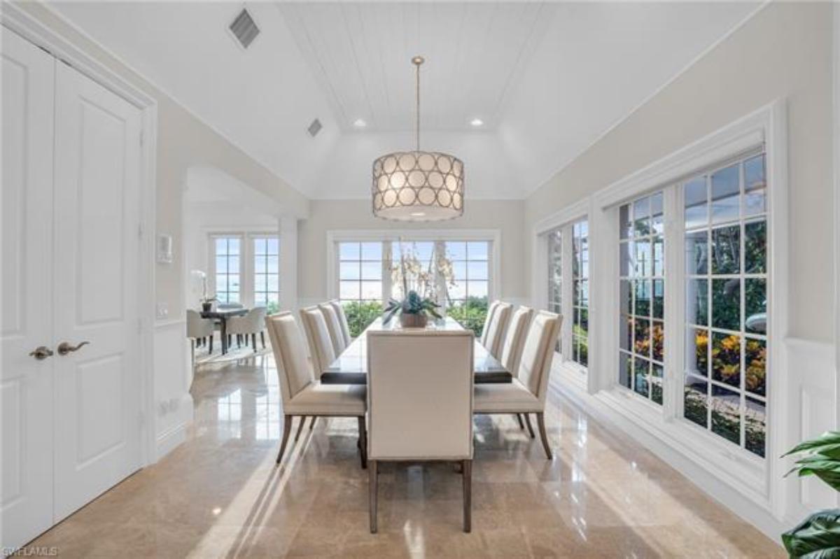 Dining room with a large table, chairs, chandelier and large glass windows.