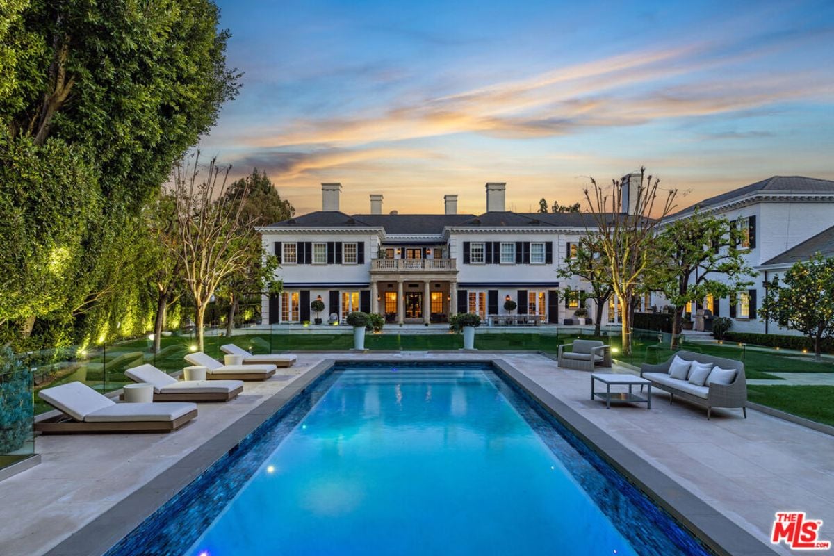 A swimming pool with chairs and a couch on the poolside.