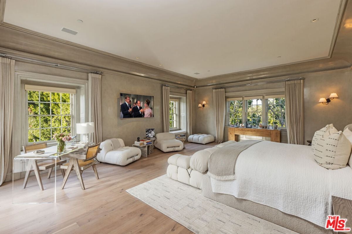 A bedroom with a bed, windows, couch, TV, desk, and chair.