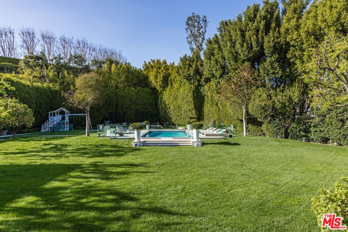 A backyard with a swimming pool, playground, and trees.