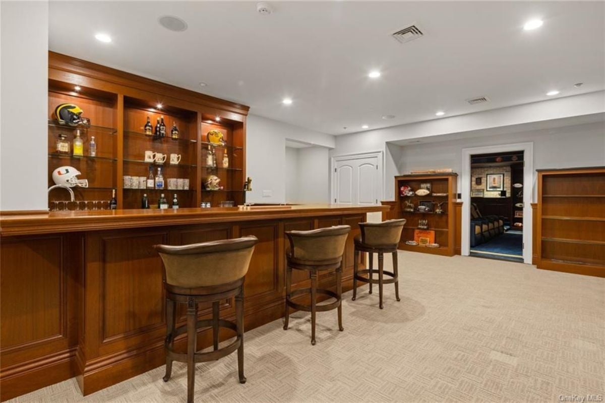A bar with a countertop, chairs, and shelves filled with liquor.