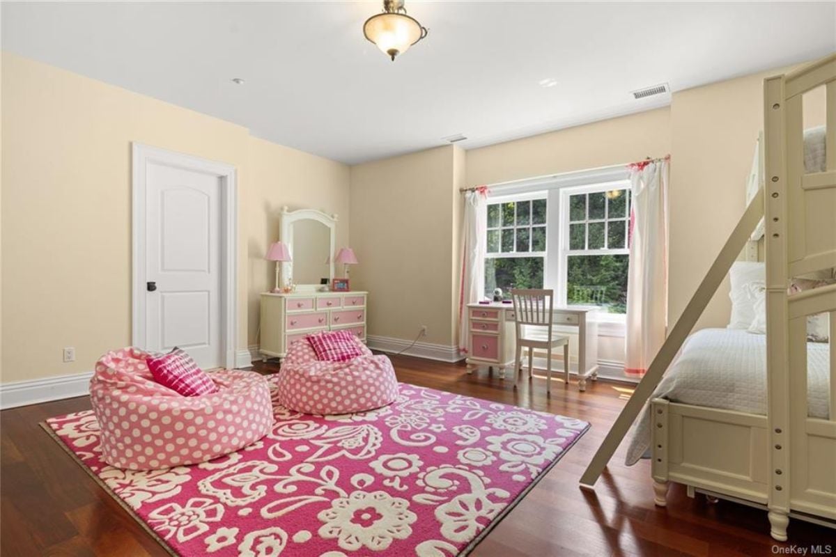 A bedroom with a double deck, a window, a desk, chairs, a rug, and bean bag chairs.