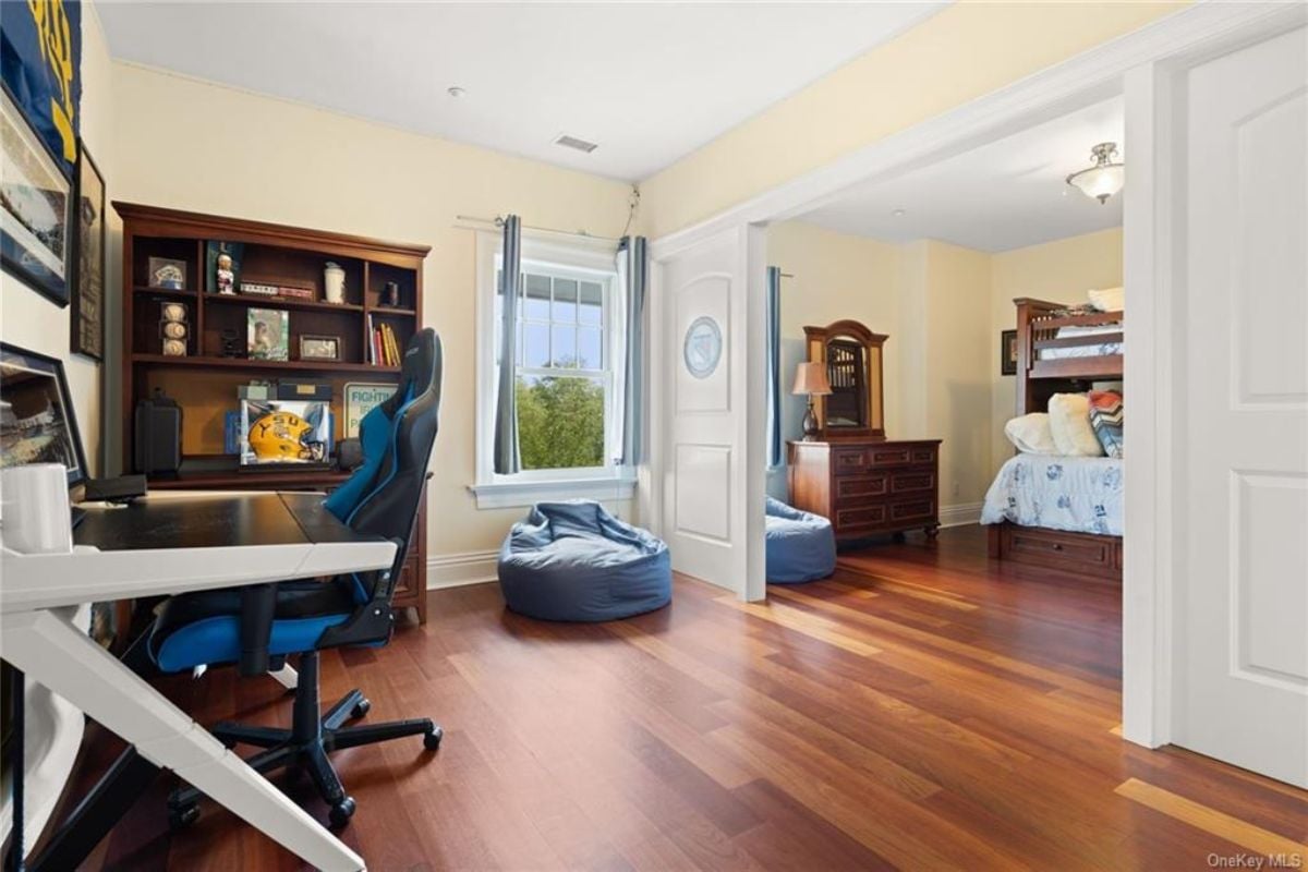 A bedroom with a desk, a chair, a shelf, a window, and a wooden floor.