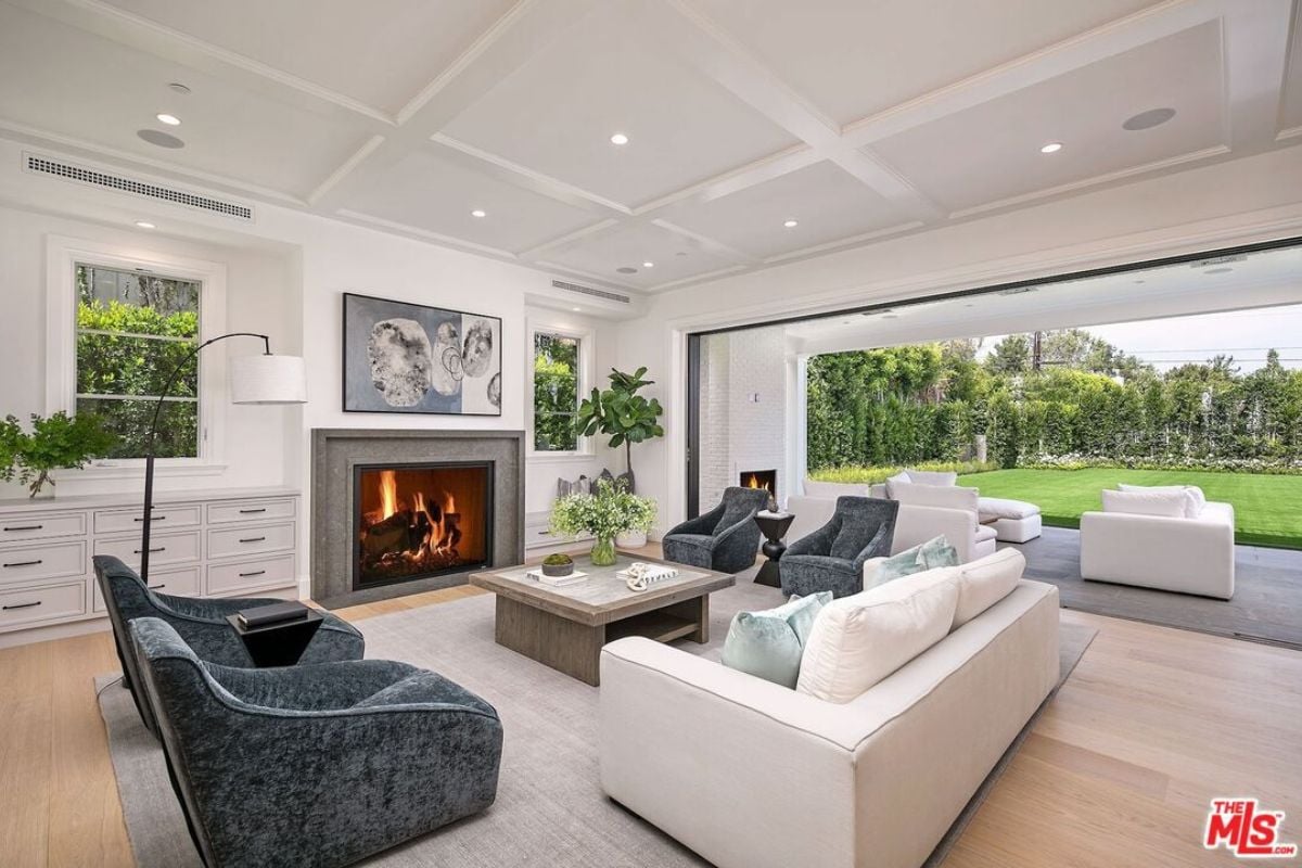 A living room with a fireplace, vaulted ceiling, painting, cabinets, houseplants, couches, and a center table.