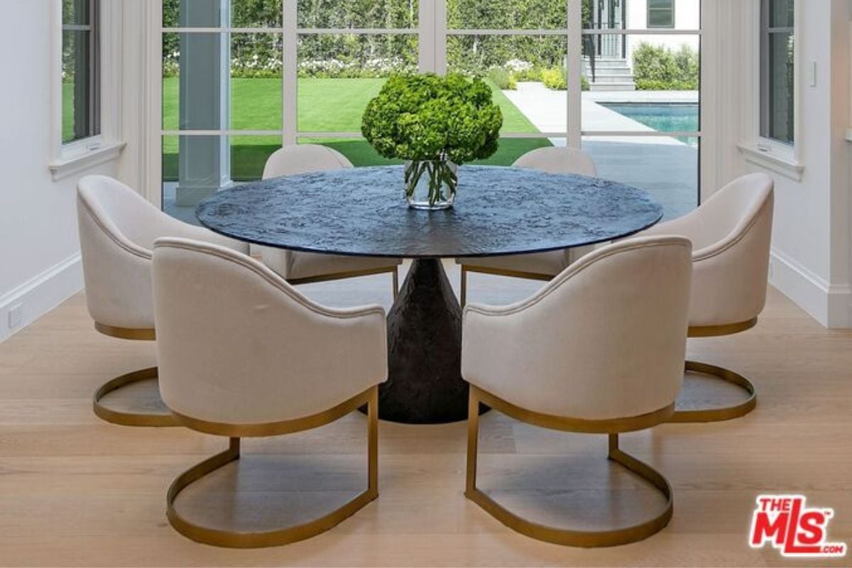 A dining area with a table adorned with a vase surrounded by white chairs.
