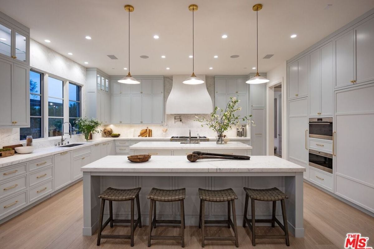 A kitchen with an island, chairs, countertops, sink, cabinets, and kitchen appliances.