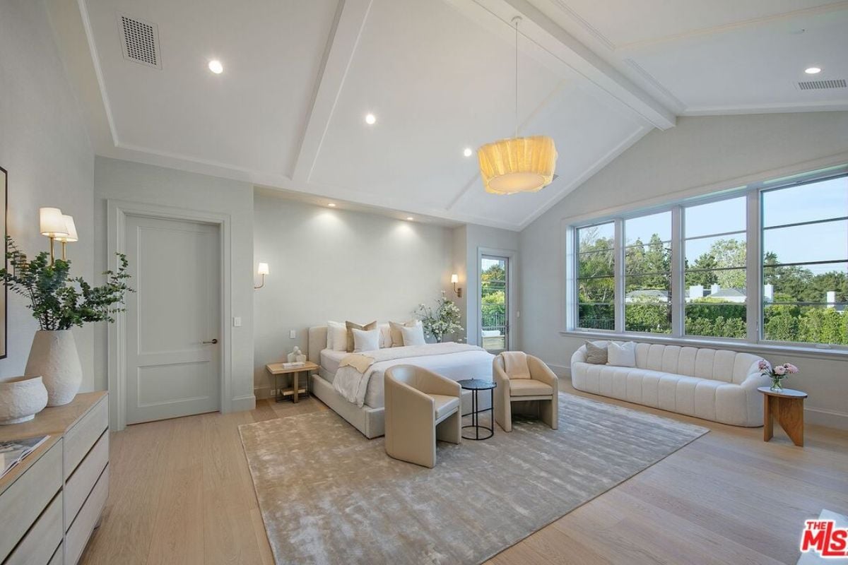 A bedroom with a bed, side table, couch, chairs, windows, vases, and a cabinet.