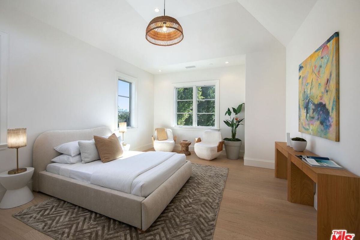 A bedroom with a nightstand, bed, painting, vaulted ceiling, and chairs.
