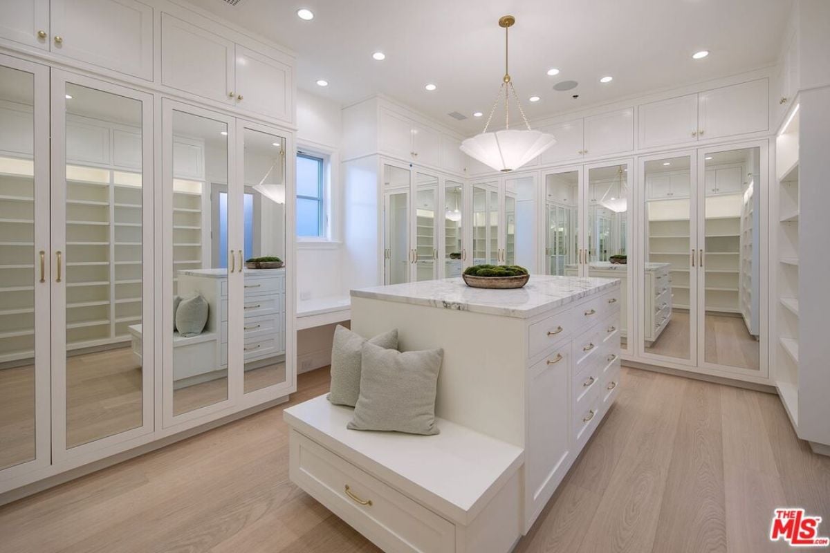 A walk-in closet with wooden floor, center island, white shelves, and cabinets.