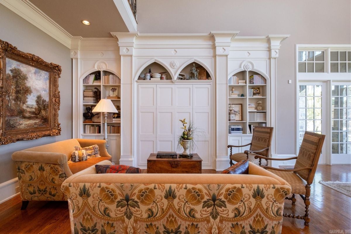 A living room with a painting, shelves, couches, chairs, and a center table.