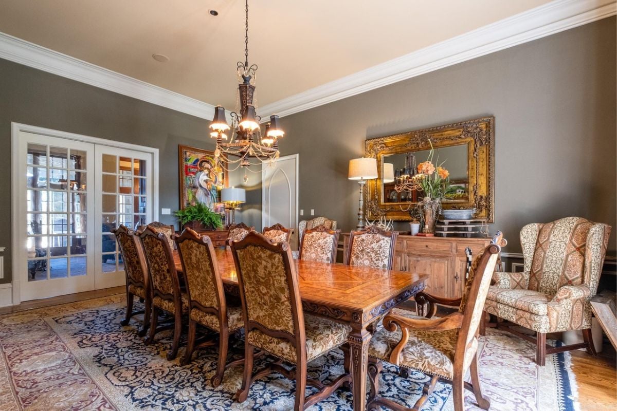 A dining room with a rug, chandelier, mirror, and dining table surrounded by chairs.