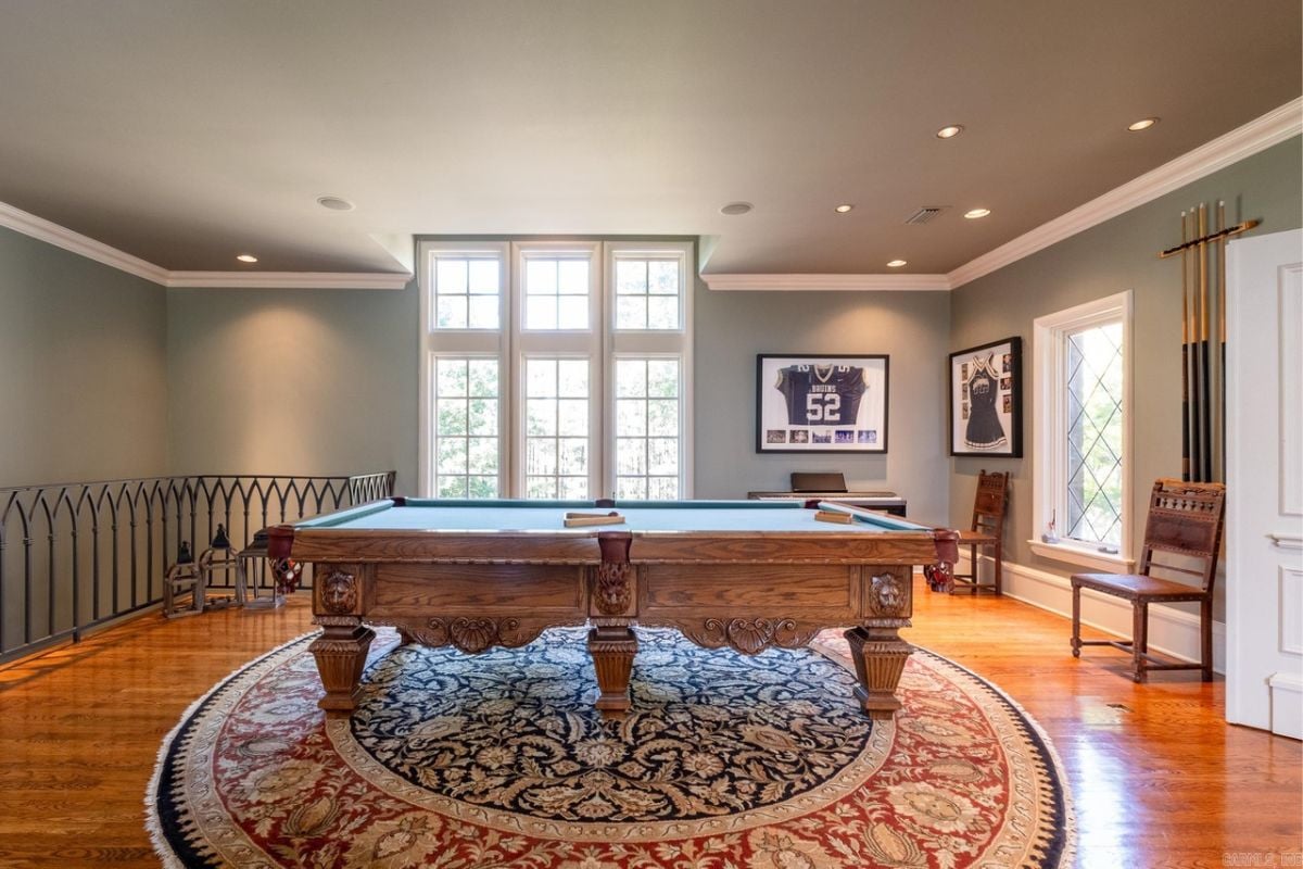 A game room with wooden floor, rug, window, and pool table.
