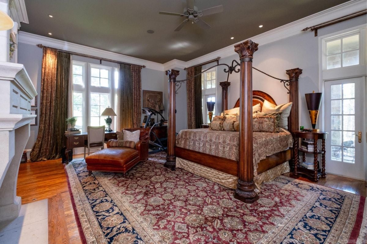 A bedroom with a bed, rug, fireplace, nightstand, windows, chairs, and treadmill.