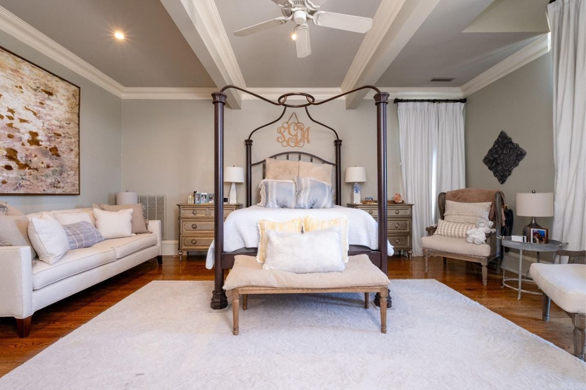 A bedroom with a bed, couches, nightstand, painting, and ceiling fan.