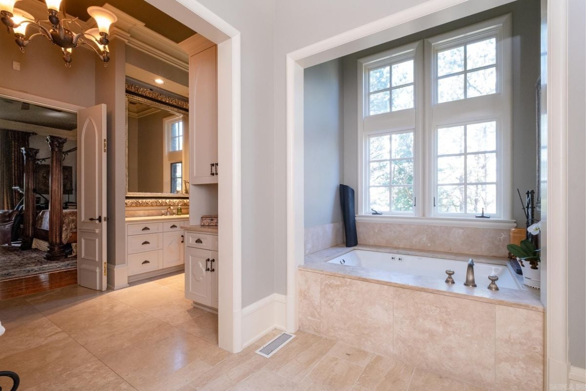 A bathroom with tiled floor, window, and square bathtub.