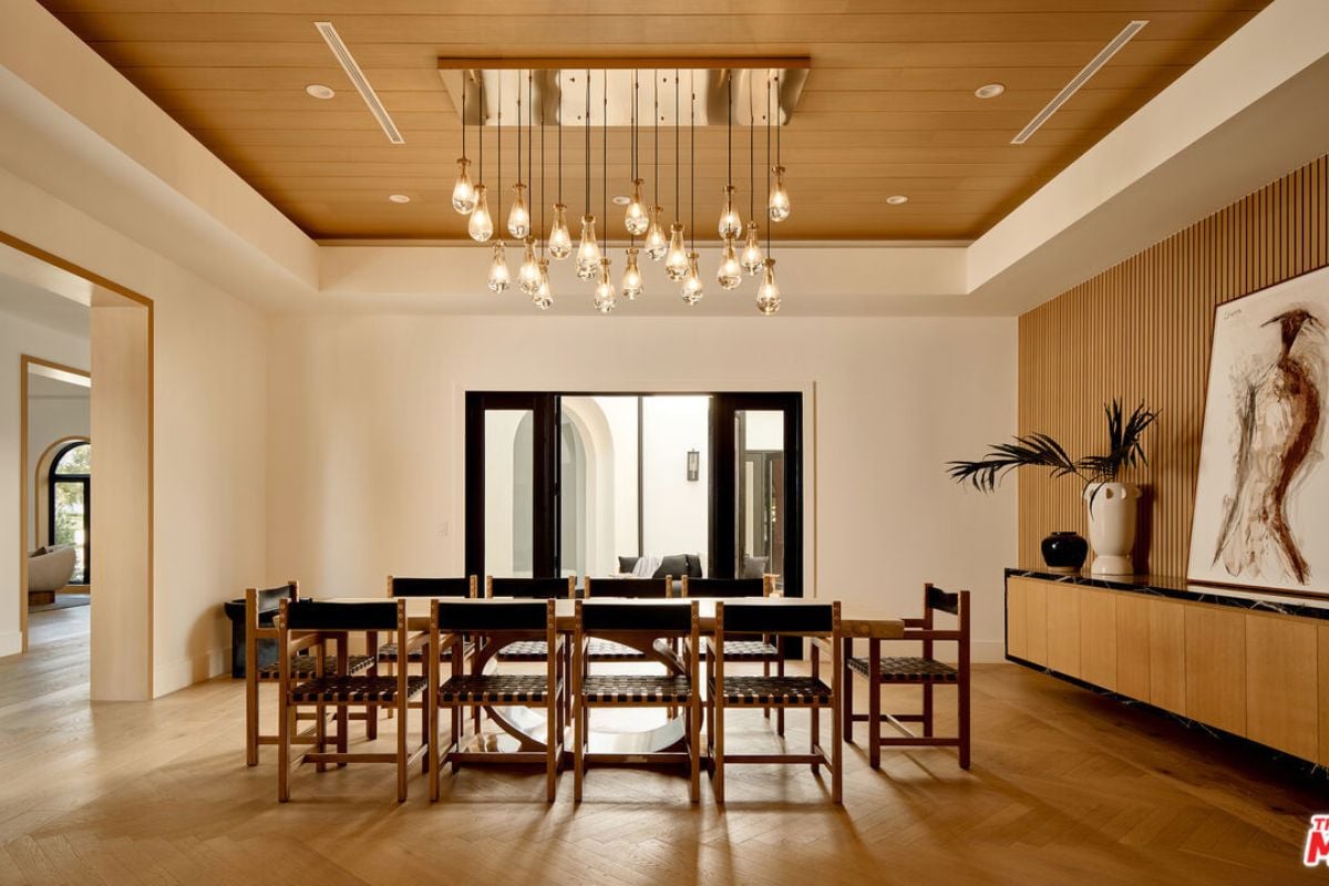 A dining room with a wooden ceiling, lighting, a painting, and a dining table surrounded by chairs.