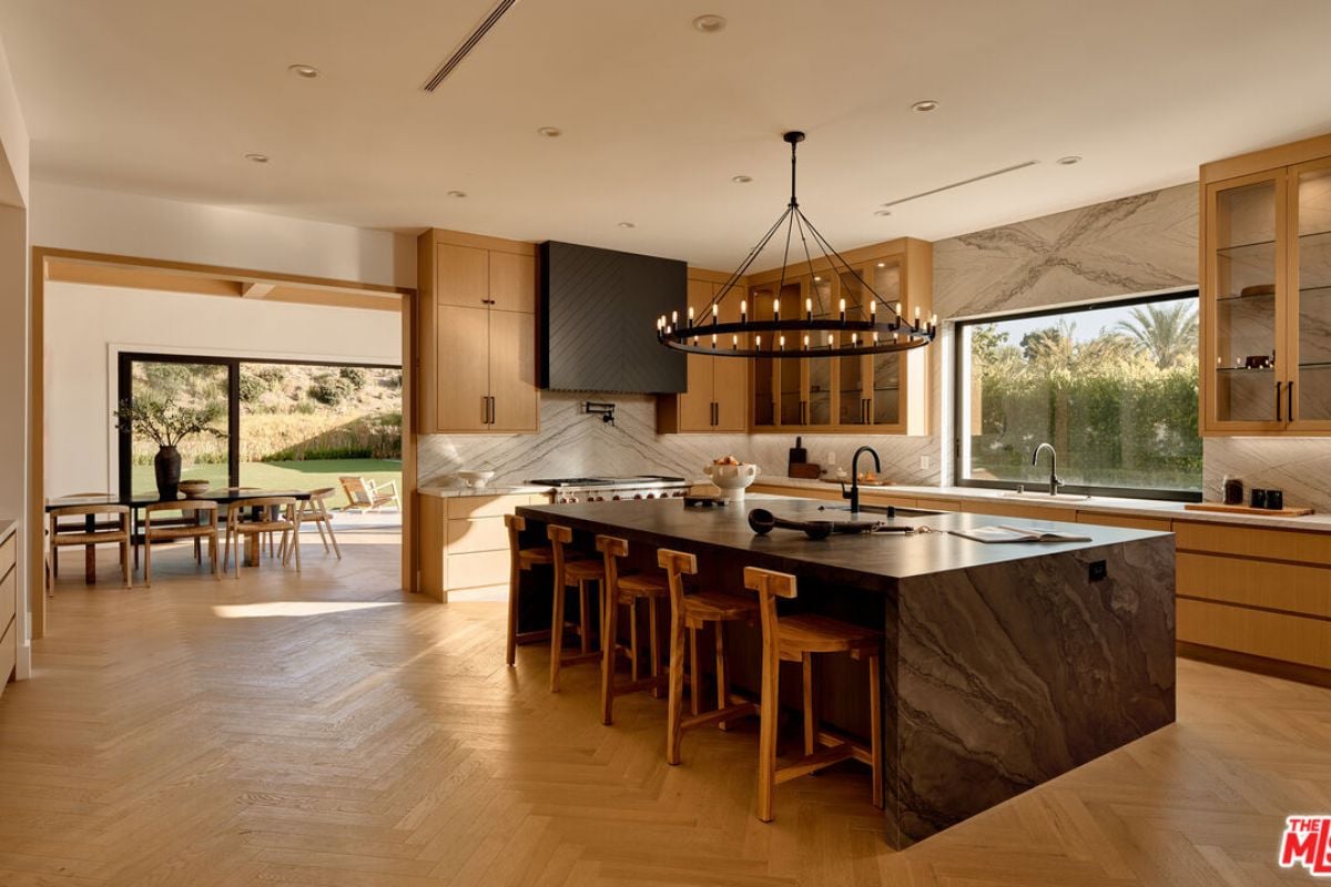 A kitchen with a center island, chairs, countertop, sink, window, cabinets, and kitchen appliances.