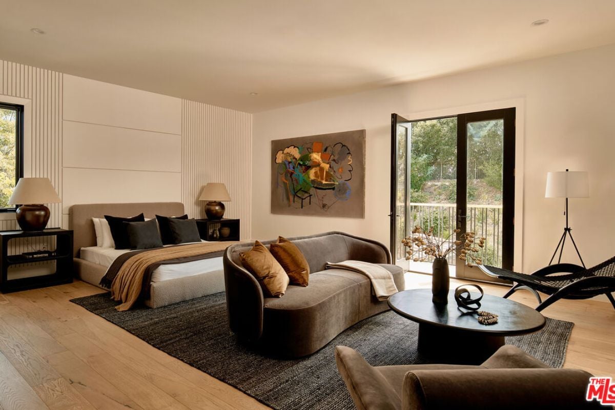 A bedroom with a bed, side table, painting, rug, couch, chair, and coffee table.