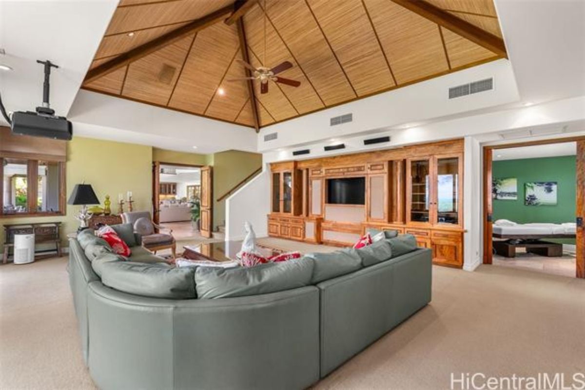 A living room with a vaulted ceiling, shelves, TV, and gray couches with pillows.