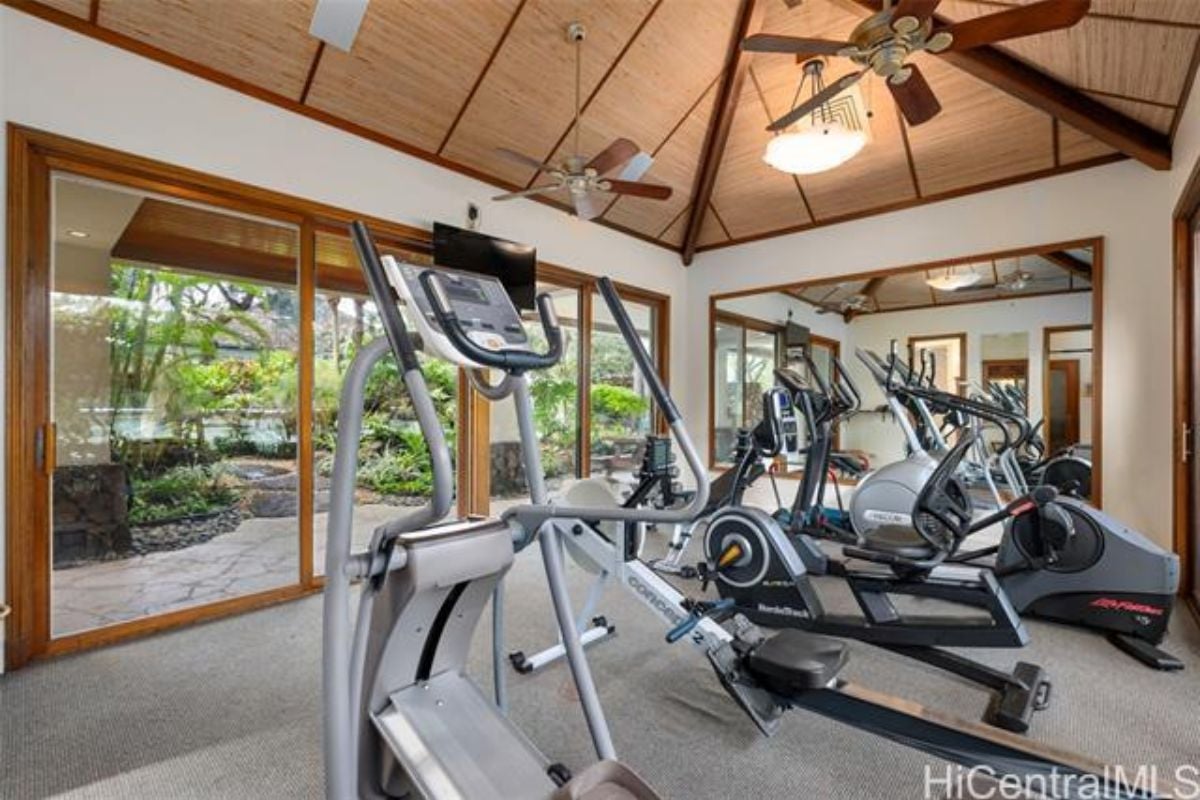 A home gym with a vaulted ceiling, ceiling fan, mirror, and gym equipment.