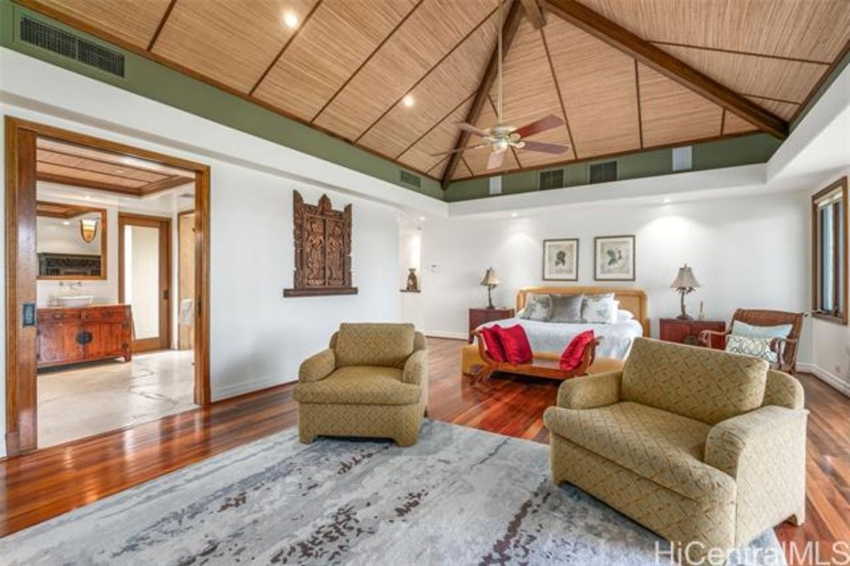 A bedroom with a bed, vaulted ceiling, ceiling fan, wooden floor, and chairs.