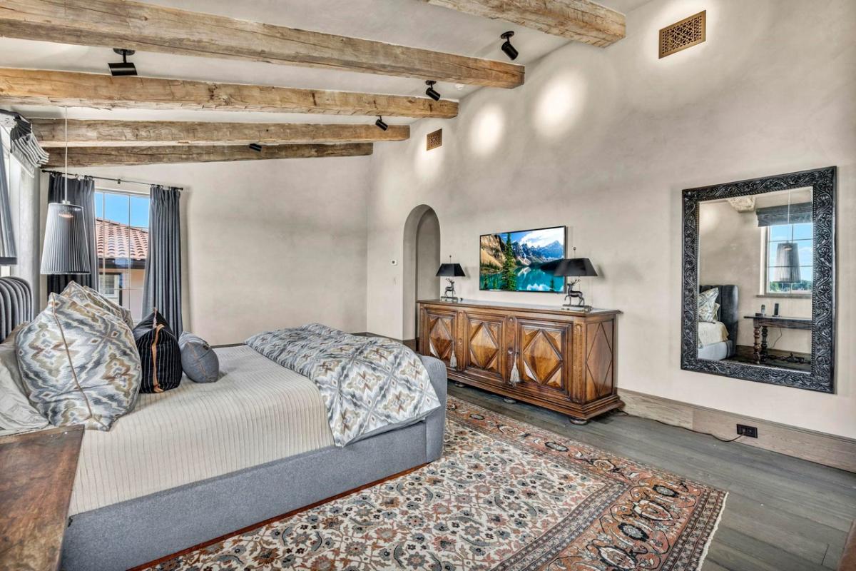 Bedroom with wood ceiling beams, hardwood floors and glass windows.