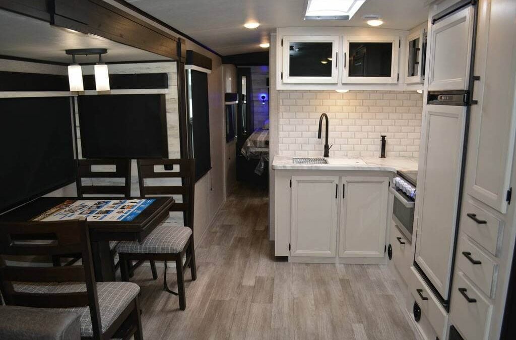 Dining area and kitchenette illuminated by warm pendants, recessed lights, and a skylight.