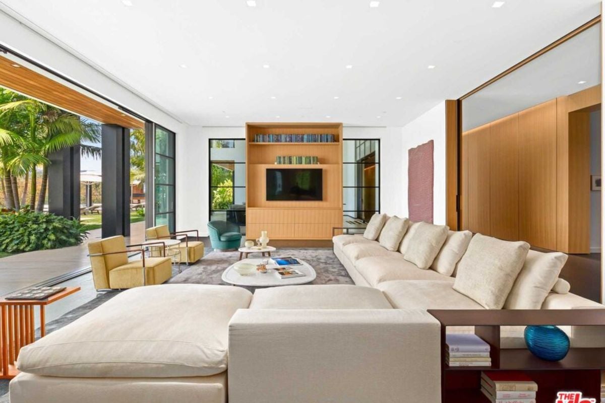 A living room with a TV, couch with pillows, chairs, center table, and a large glass sliding door.