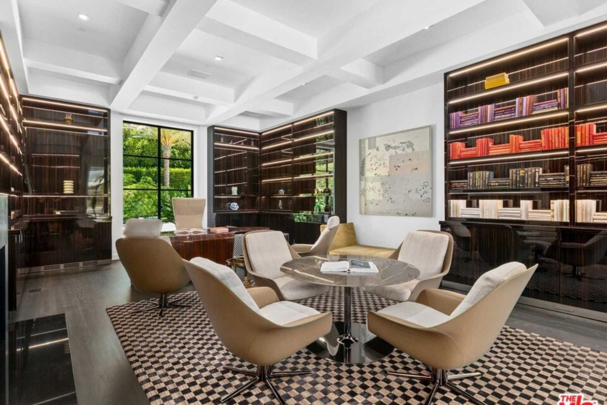 A home office with a rug, shelves, vaulted ceiling, desk, table, and chairs.