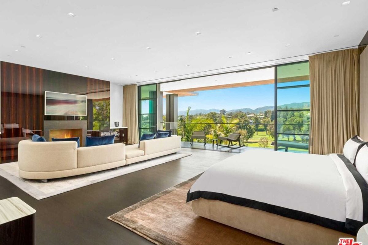 A bedroom with a bed, fireplace, couch, TV, and large sliding door connected to the balcony.