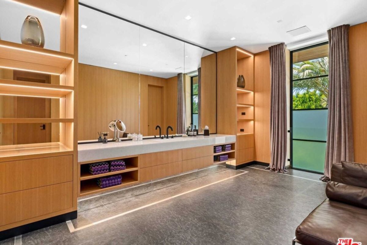A bathroom with countertop, sink, mirror, shelves, and cabinets.
