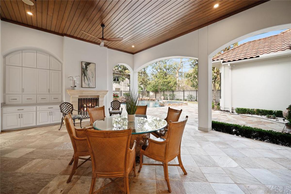Covered patio with round glass table, chairs and a fireplace.