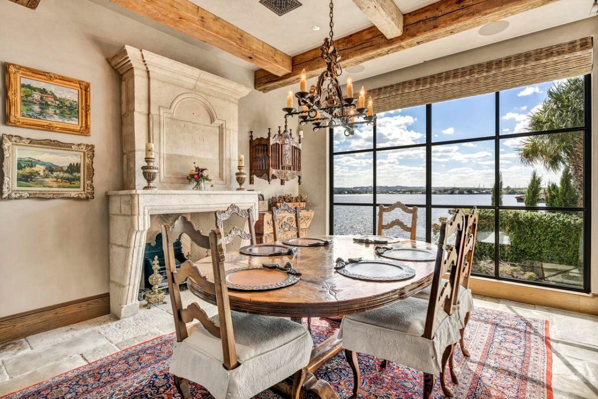 Dining room with a chandelier, glass walls and wood ceiling beams.