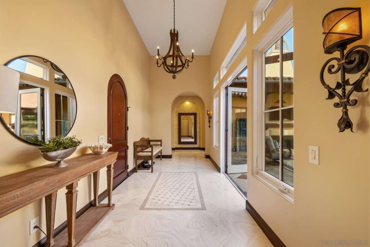 An entry hall with a mirror, chandelier, table, and bench.