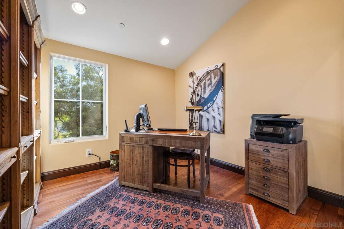 A home office with wooden floors, a window, shelves, a cabinet, a desk, and a chair.