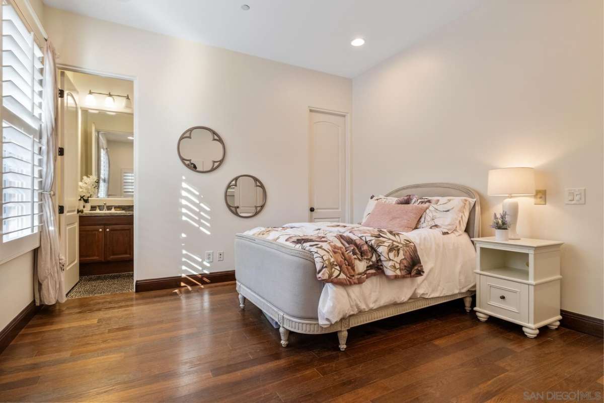 A bedroom with a bed, wooden floor, nightstand, and windows.