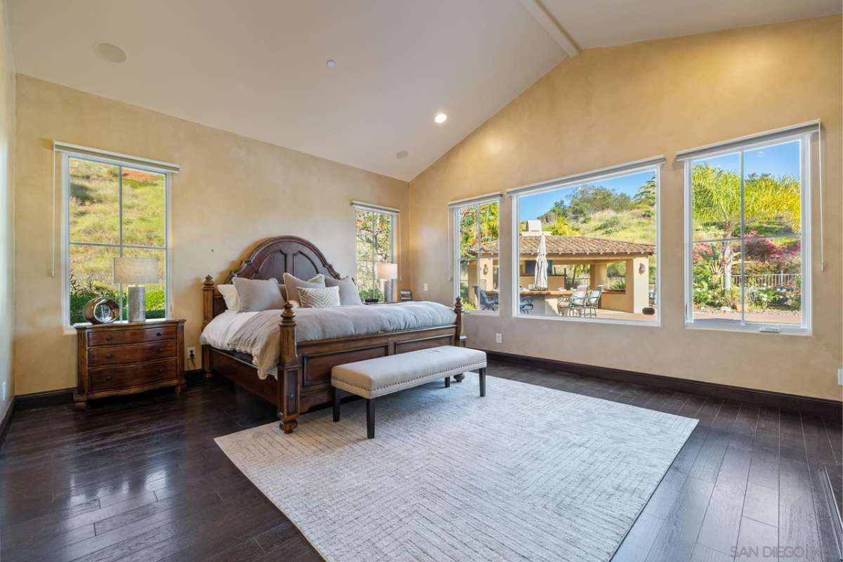 A bedroom with a bed, hardwood floor, nightstand, and windows.