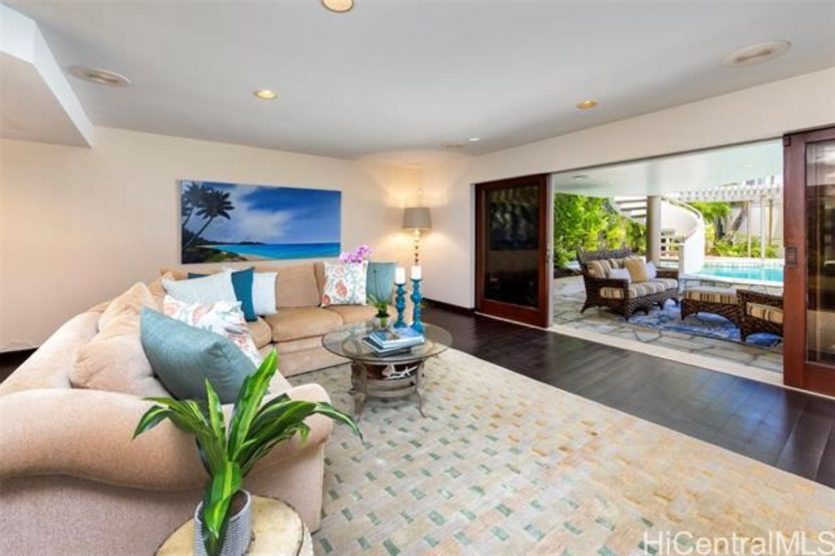 A living room with hardwood floors, a rug, a potted plant, a couch, a center table, and a TV.