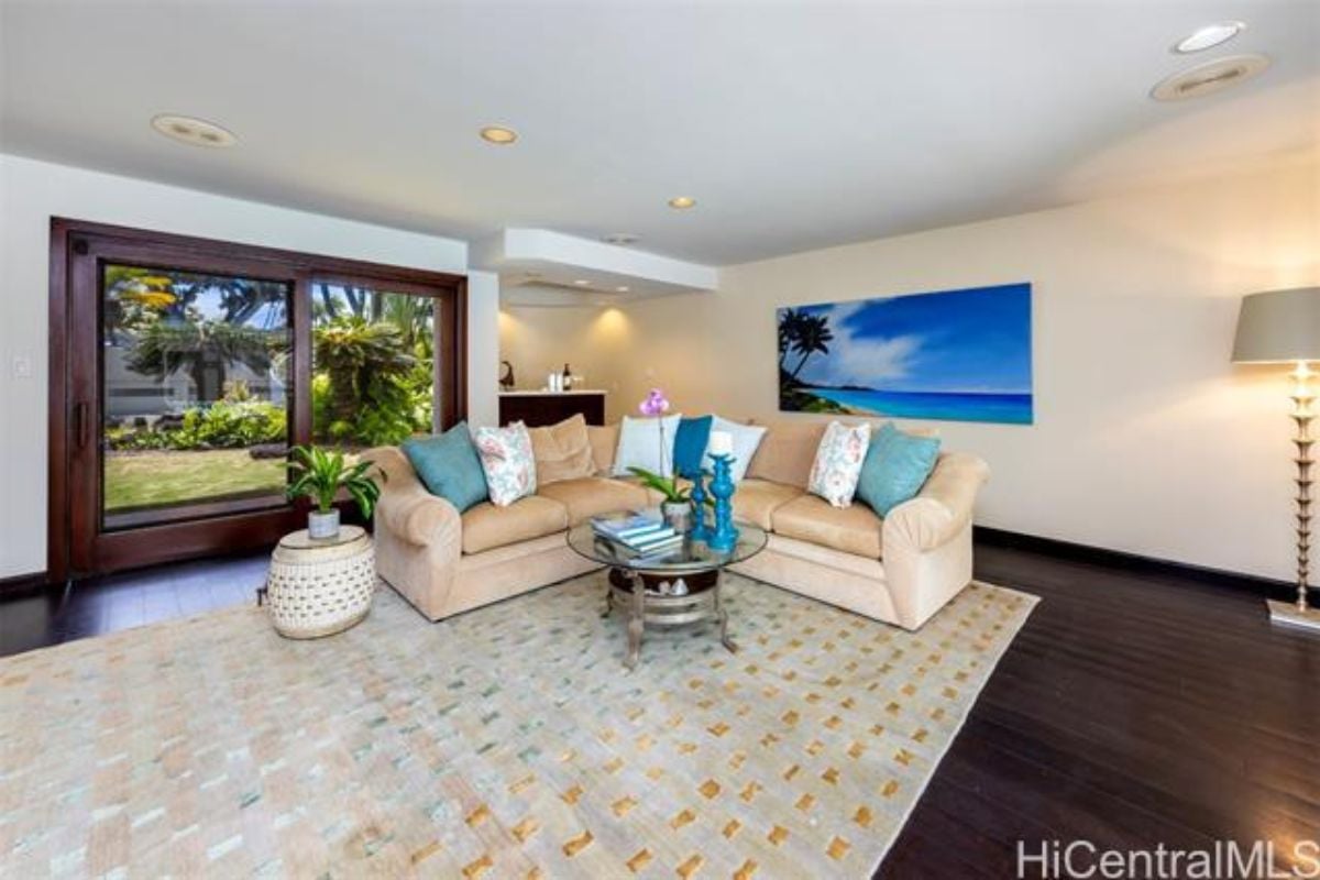 A living room with hardwood floors, a rug, a potted plant, a couch, a center table, and a TV.