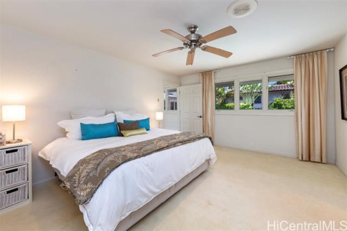 A bedroom with a bed, windows, ceiling fan, and nightstand.