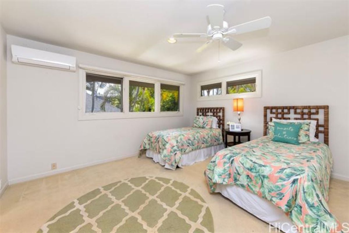 A bedroom with two beds, windows, a ceiling fan, and a rug.