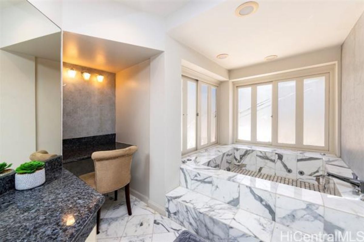 A bathroom with a countertop, chairs, tiled floor, windows, and bathtub.