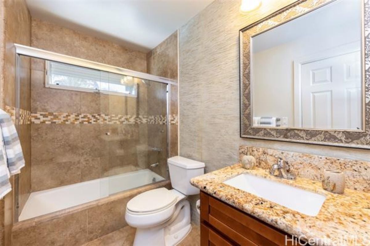 A bathroom with a countertop, sink, mirror, cabinet, bathtub and toilet.