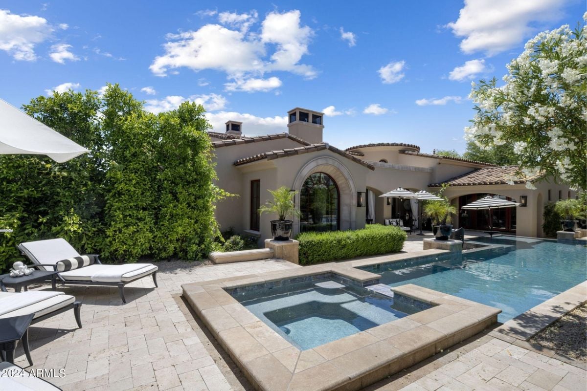 A swimming pool with a jacuzzi, surrounded by plants and chairs on the poolside.