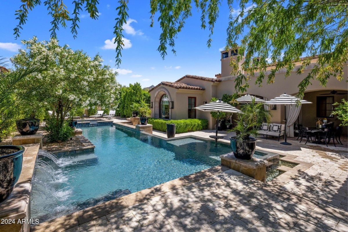 A swimming pool with a jacuzzi, surrounded by plants and chairs on the poolside.