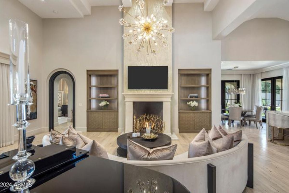 A living room with a piano, TV, fireplace, chandelier, shelves, couch, and center table.