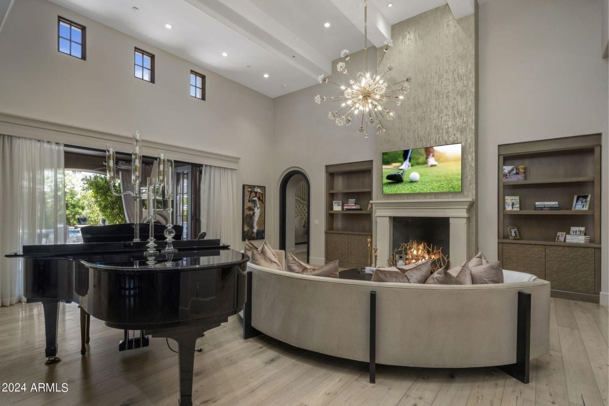 A living room with a piano, TV, fireplace, chandelier, shelves, couch, and center table.